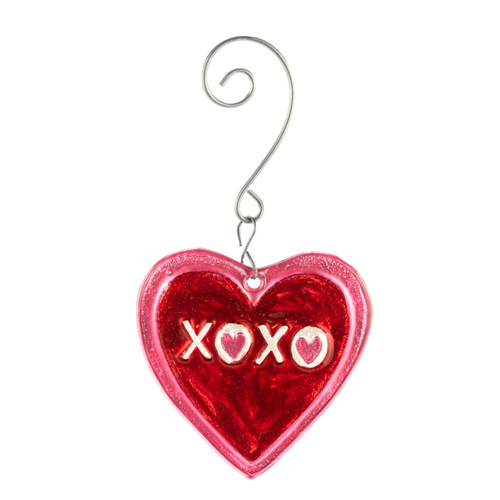 A red heart shaped glass ornament that says "XOXO" and is on a curved silver metal hanger.