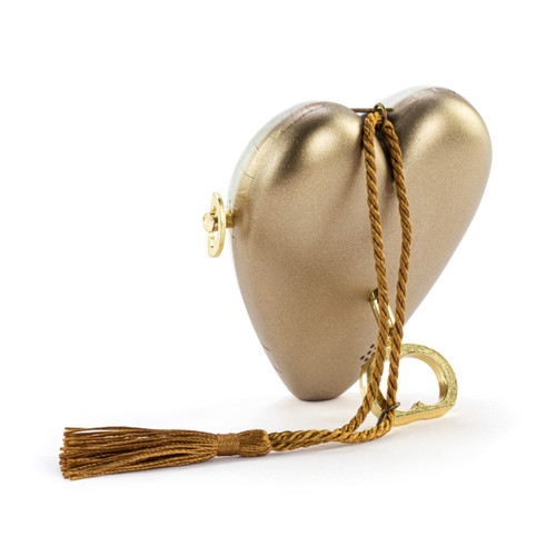 Back view showing the heart propped on the key for a white heart shaped musical sculpture with the saying "Our First Christmas" with an illustration of two full stockings. The heart has a gold tassel and gold key attached.