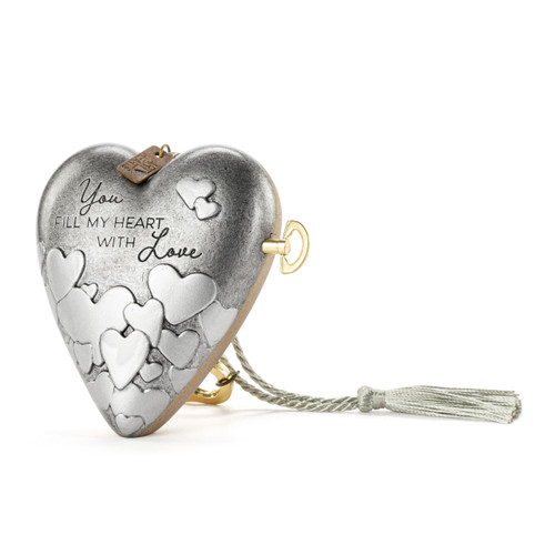A silver heart shaped musical sculpture with a heart pattern that reads "You Fill My Heart With Love". The heart has a silver tassel and gold key attached, displayed angled to the left.