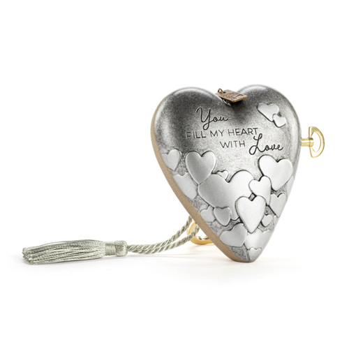 A silver heart shaped musical sculpture with a heart pattern that reads "You Fill My Heart With Love". The heart has a silver tassel and gold key attached, displayed angled to the right.