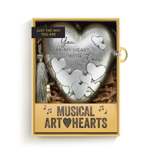 A silver heart shaped musical sculpture with a heart pattern that reads "You Fill My Heart With Love". The heart has a silver tassel and gold key attached, displayed in a packaging box.