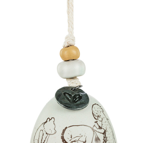 Detail view of the beads on a mini white and gray bell with an image of Christopher Robin reattaching Eeyore's tail. There are beads and a metal token at the top of the bell.