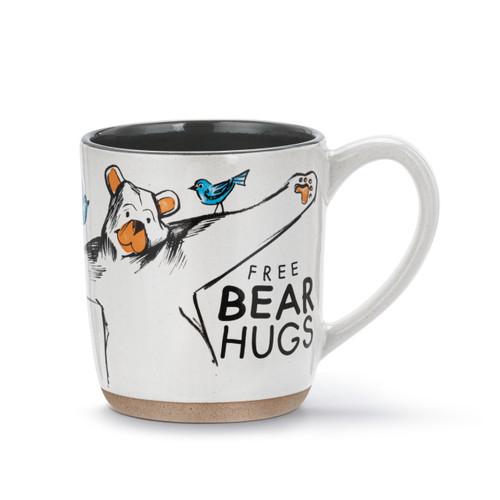 A white ceramic mug with a tan textured base. There is a drawing of a bear about to give a hug and the mug says "Free Bear Hugs".