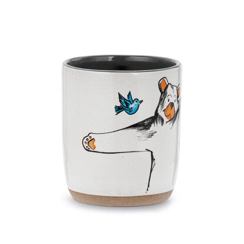 Side view of a white ceramic mug with a tan textured base. There is a drawing of a bear about to give a hug and the mug says "Free Bear Hugs".