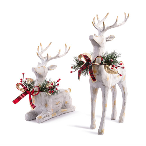Two large carved wood reindeer figures painted white. One is standing and the other is kneeling. Each has a holly and ribbon wreath around its neck.