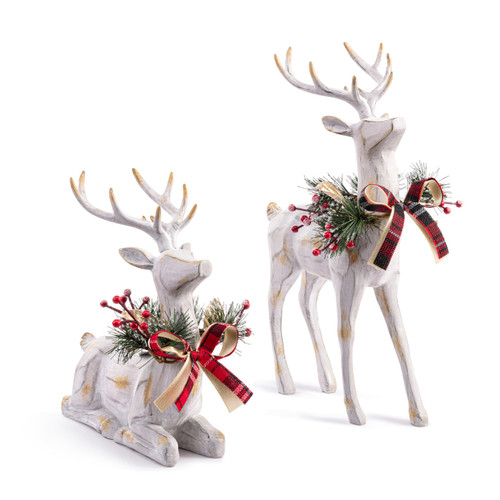 Two large carved wood reindeer figures painted white. One is standing and the other is kneeling. Each has a holly and ribbon wreath around its neck, displayed angled to the right.