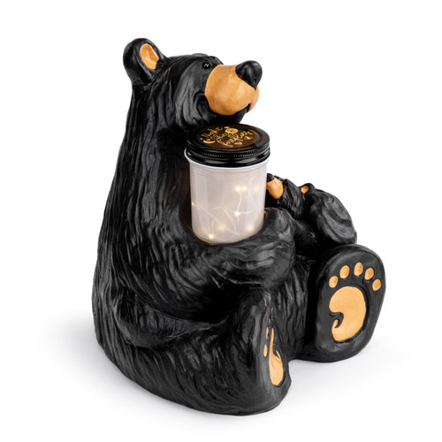 An adult black bear sitting holding a jar of fireflies in his right arm and a curious small bear in his left arm, displayed angled to the right.