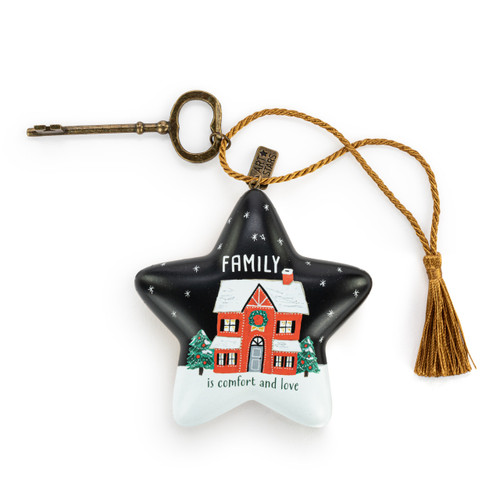 A black and white star shaped sculpture with the saying "Family is comfort and love" with an illustration of a home in the snow. The star has a gold tassel and gold key attached.