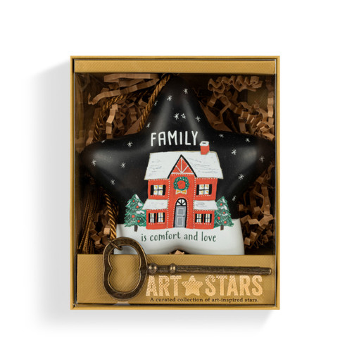 A black and white star shaped sculpture with the saying "Family is comfort and love" with an illustration of a home in the snow. The star has a gold tassel and gold key attached, displayed in a packaging box.