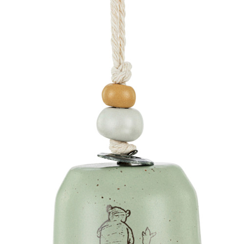 Detail view of the beads on a mini tan and green bell with an image of Pooh and Piglet walking together. There are beads and a metal token at the top of the bell.