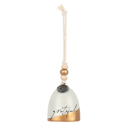 A mini cream and gold bell with the word "grateful" on the front. There are beads and a metal token at the top of the bell.