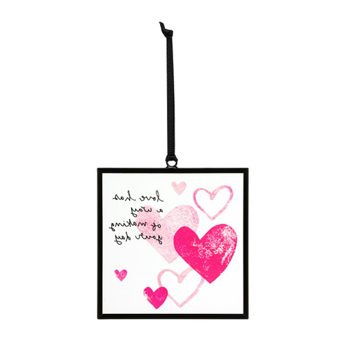 Back view of a small square shaped sun catcher with illustrated pink hearts and the saying "love has a way of making your day".