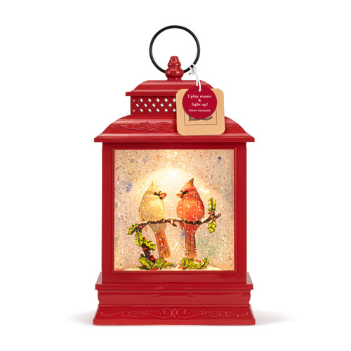A red lit musical lantern with the image of a cardinal pair sitting on a branch in the snow, displayed with a product tag attached.