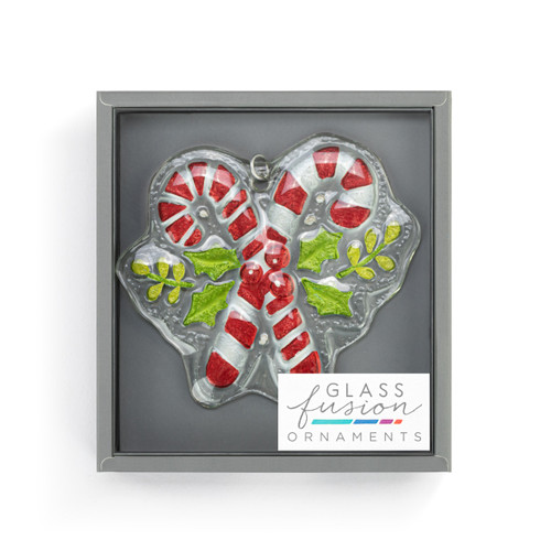 A glass ornament of two crossed candy canes and holly leaves with a curved silver hanger, displayed in a packaging box.