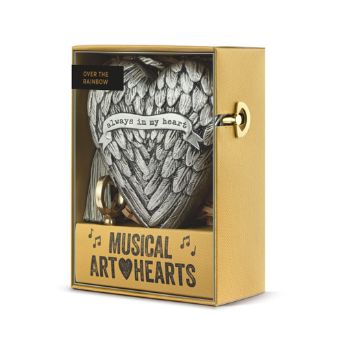 A silver heart shaped musical sculpture with a wing pattern that reads "always in my heart". The heart has a silver tassel and gold key attached, displayed in a packaging box angled to the left to show the winder.
