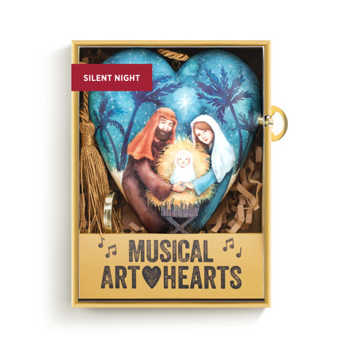 A blue heart shaped musical sculpture with an image of the holy family. The heart has a gold tassel and gold key attached, displayed in a packaging box.