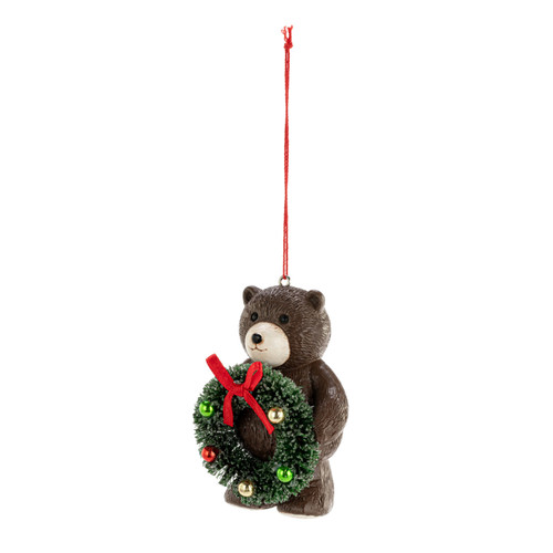 A small brown teddy bear ornament holding a green decorated wreath, displayed angled to the left.