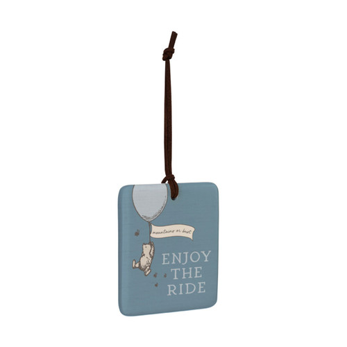A square blue hanging tile magnet ornament that says "Enjoy The Ride" with an image of Pooh hanging on a balloon that says "mountains or bust", displayed angled to the right.