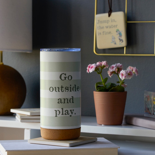 A white desk setting with a white tumbler in light green and white stripes with the saying "Go outside and play".