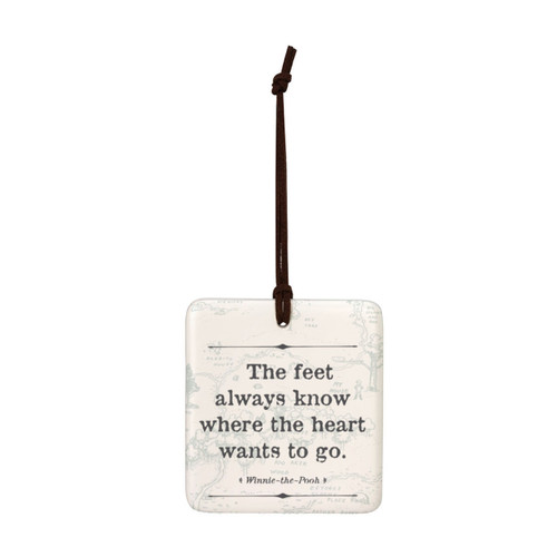 A square cream hanging tile magnet ornament that says "The feet always know where the heart wants to go", with a light image of the hundred acre wood in the background.