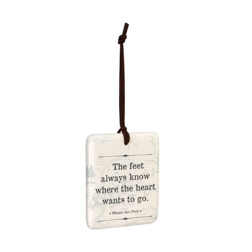 A square cream hanging tile magnet ornament that says "The feet always know where the heart wants to go", with a light image of the hundred acre wood in the background, displayed angled to the right.