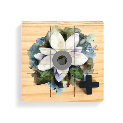 A square wood board for tic tac toe with a watercolor image of a white magnolia, displayed with a gray O and black X on top.