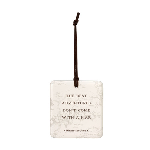 A square cream hanging tile magnet ornament that says "The Best Adventures Don't Come With A Map", with a light image of the hundred acre wood in the background.