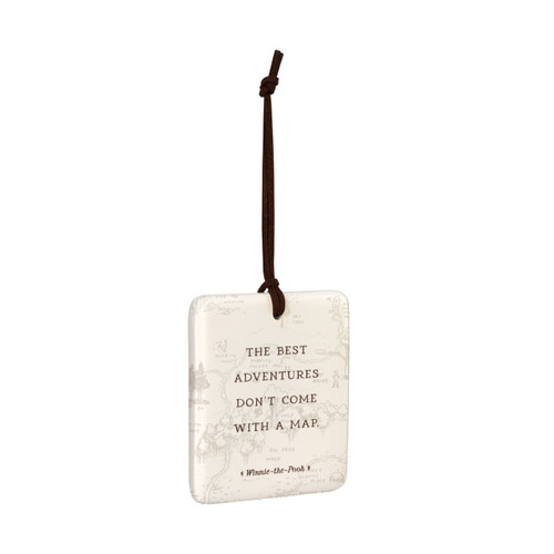 A square cream hanging tile magnet ornament that says "The Best Adventures Don't Come With A Map", with a light image of the hundred acre wood in the background, displayed angled to the right.