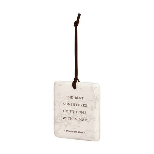 A square cream hanging tile magnet ornament that says "The Best Adventures Don't Come With A Map", with a light image of the hundred acre wood in the background, displayed angled to the left.