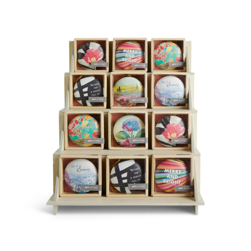 A four tier light wood displayer with an assortment of round ArtLifting ornaments in packaging boxes.