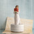 Faceless woman figurine wearing white holding red flowers standing on round white plaque - background is a music sheet under her with blue background