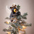 Close view of small black bear figurine clinging to green christmas tree with ornaments