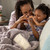 A mother and a child cuddling on a white sofa, with a purple "Mom and Me Cuddle Blanket".