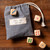 A close up image of a black and white bag drawstring bag placed on a wooden table with five colorful dice.