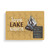 A rectangular wood 24 piece postcard puzzle with a bonfire and the saying "Love Lake Nights" on a dark yellow background with a product information tag attached.
