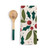 A cream kitchen towel with holly leaves and red berries next to a wood spoon with a green handle.