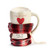 Cream stoneware handled travel mug with a red base and cream travel lid. The mug has a red heart above which says "mug of merry", displayed with the drawstring plaid bag halfway up the mug.