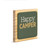 A square wood plaque with a dark green tile that says "Happy Camper", displayed angled to the right.