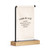 A cream canvas sign with black writing that says "i can & will Start Each Day With A Grateful Heart" hanging on a black metal stand with a wood base, displayed angled to the right.