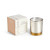 A candle in a white and gold round glass container sitting next to a peach and white packaging box. The candle name is Enchanted Mornings.