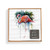 A square white wood board for tic tac toe with a watercolor image of a flamingo, displayed in a packaging box.