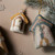 Top down view of two different plush and felt ornaments of Baby Jesus and the holy family, displayed by frosted tree branches and a wrapped gift.