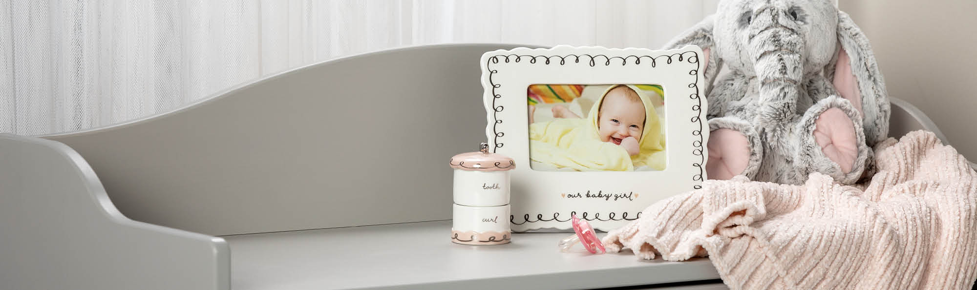 Frame, Tooth Box, Stuffed Elephant, and soft blanket setting on a white dresser