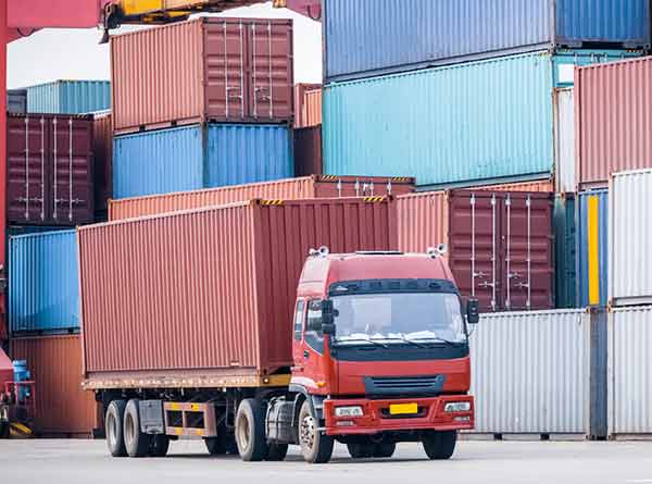 Truck driving in front of a row of large shipping containers