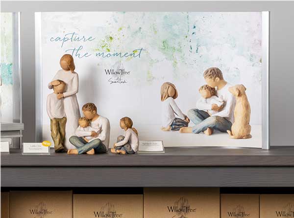 Sign that reads Capture the Moment with Willow Tree hand carved figurines setting in front