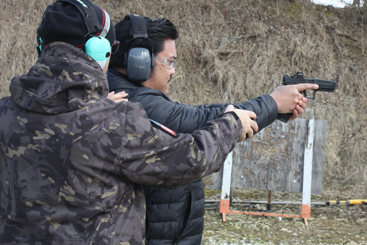 man helping another man aim firearm