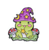 Magic Witch Frog enamel pin sitting on green grass with bright red mushrooms on either side holding a want. HP-36
