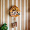 Decorative view of the Rheinberg Musical Chalet German Quartz Cuckoo Clock on brown and white stripped wall with green plants