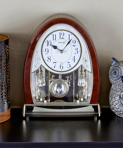 RHYTHM musical mantle clock featuring a classic design with elegant faux wood finish, round face, and ornate gold accents. The clock has a stylish, crystal-embedded swinging pendulum. 4RJ636WD23 RHYTHM musical mantle clock featuring a classic design with elegant faux wood finish, round face, and ornate gold accents. The clock has a stylish, crystal-embedded swinging pendulum. 4RJ636WD23