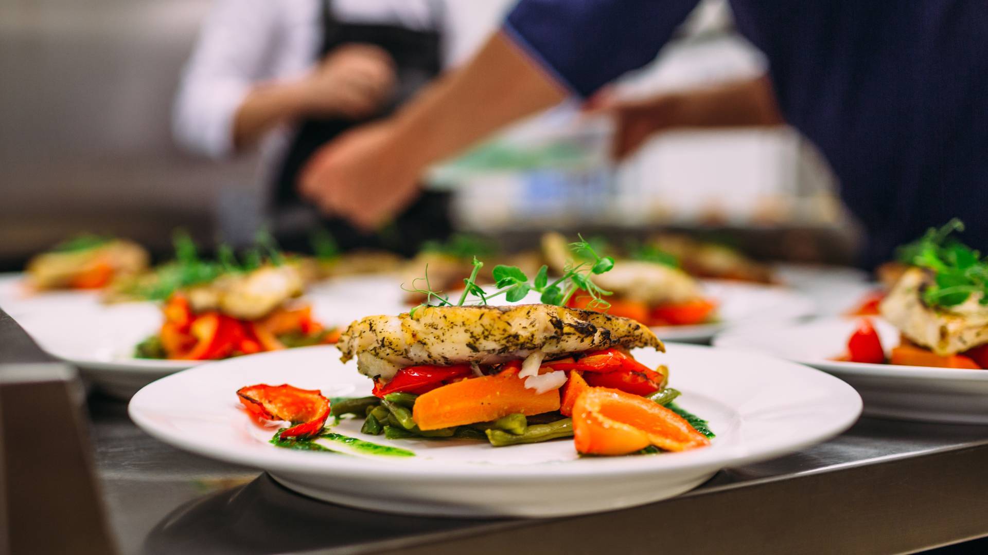  Several rows of prepared dishes in the kitchen of a restaurant with chicken and vegetables including green beans and peppers.